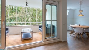 Ein modernes Zimmer mit einer Schiebetür zum Balkon, einem Essbereich mit rundem Tisch und Stühlen sowie einer hängenden Pendelleuchte.