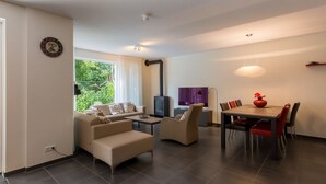 Una sala de estar moderna con un sofá, sillones, televisión y un comedor con mesa y sillas.