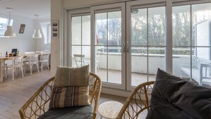 Ein heller, offener Wohnbereich mit Esstisch, Korbstühlen und einer großen Schiebeglasdoor zum Balkon.