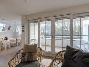 Ein heller, offener Wohnbereich mit Esstisch, Korbstühlen und einer großen Schiebeglasdoor zum Balkon.