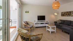 Ein modernes Wohnzimmer mit Fernseher, Korbsesseln, einer Couch und einem Balkon mit Glastüren.
