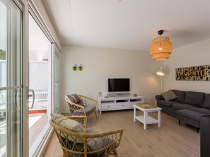 Ein modernes Wohnzimmer mit Fernseher, Korbsesseln, einer Couch und einem Balkon mit Glastüren.