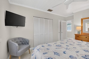 A bedroom with a bed, a chair, a dresser, a television, and a ceiling fan.