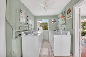 A laundry room with two washing machines, a ceiling fan, a window with a view, and a door leading outside.