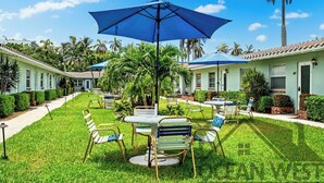 Een binnenplaats met buiten zitplaatsen, palmbomen en een blauwe parasol.
