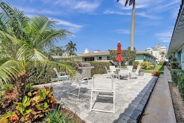 A patio area with outdoor furniture, a grill, and a pathway leading to a building.