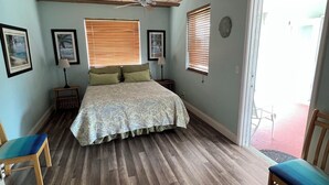 Een slaapkamer met een houten plafond, een bed met een beddengoed met patroon, twee nachtkastjes met lampen en een raam met jaloezieën.