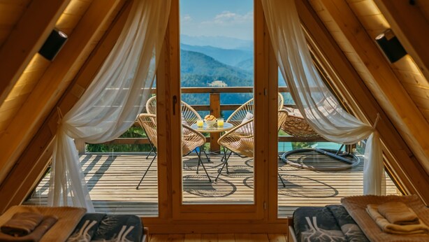 Vue intérieure d’un chalet en bois doté d’un balcon donnant sur un paysage montagneux.