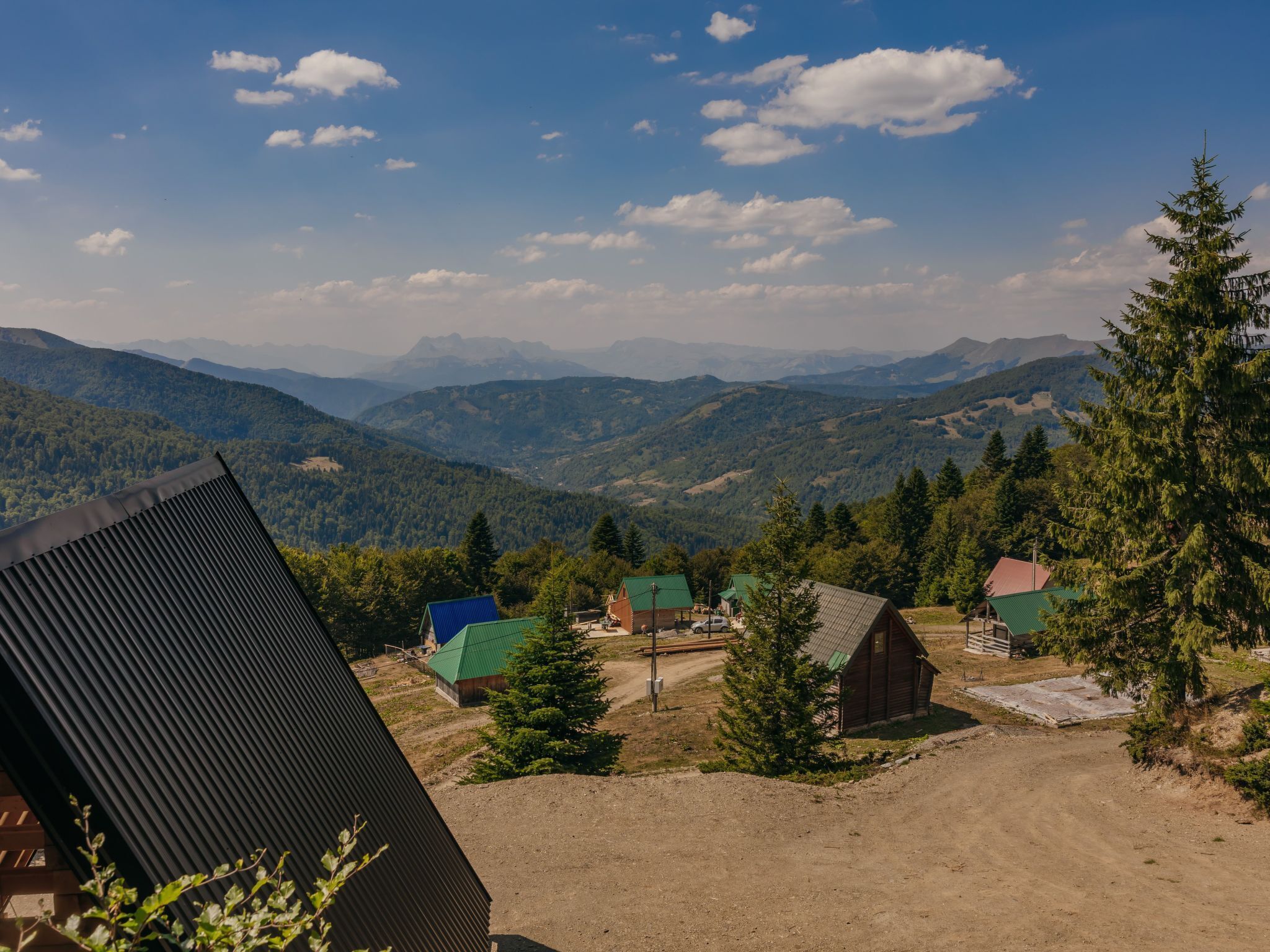 Vista de la montaña con un pequeño poblado, incluyendo una construcción con techo de metal corrugado y varias estructuras más pequeñas con tejados verdes.