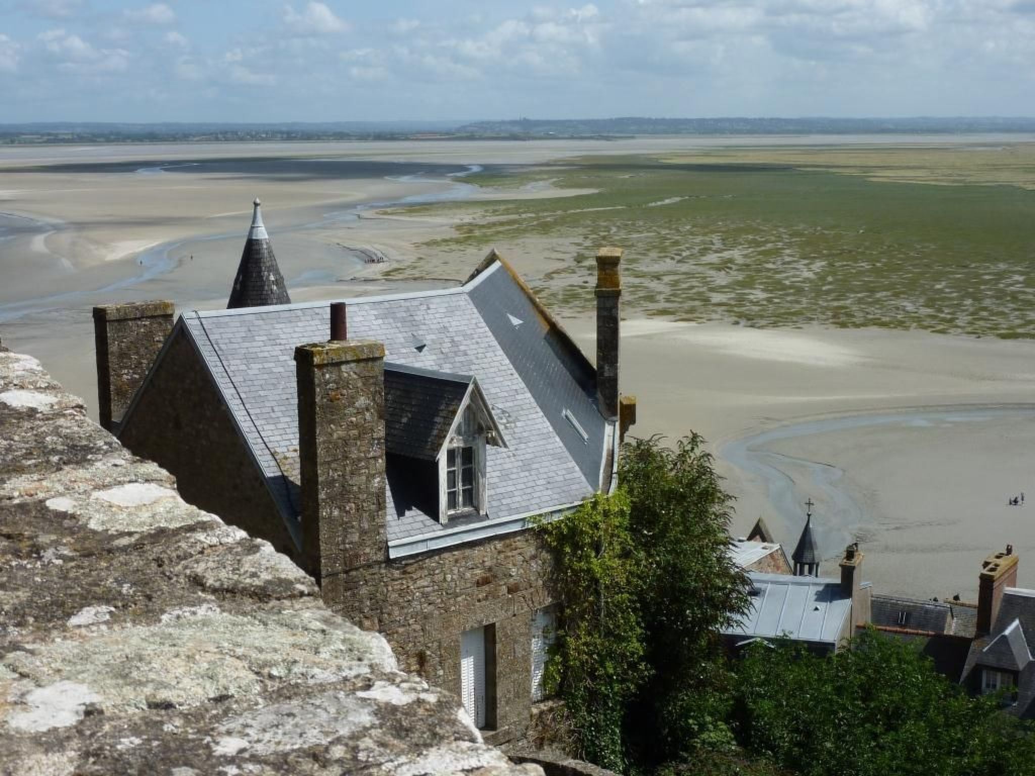 Un edificio de piedra con techo inclinado y una ventana pequeña, con vista a una playa y al agua.