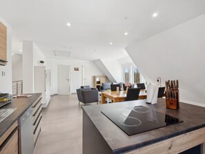 Eine moderne Küche mit Einbauherd, ein Essbereich mit Tisch und Stühlen sowie ein Ausblick ins Freie durch große Fenster.