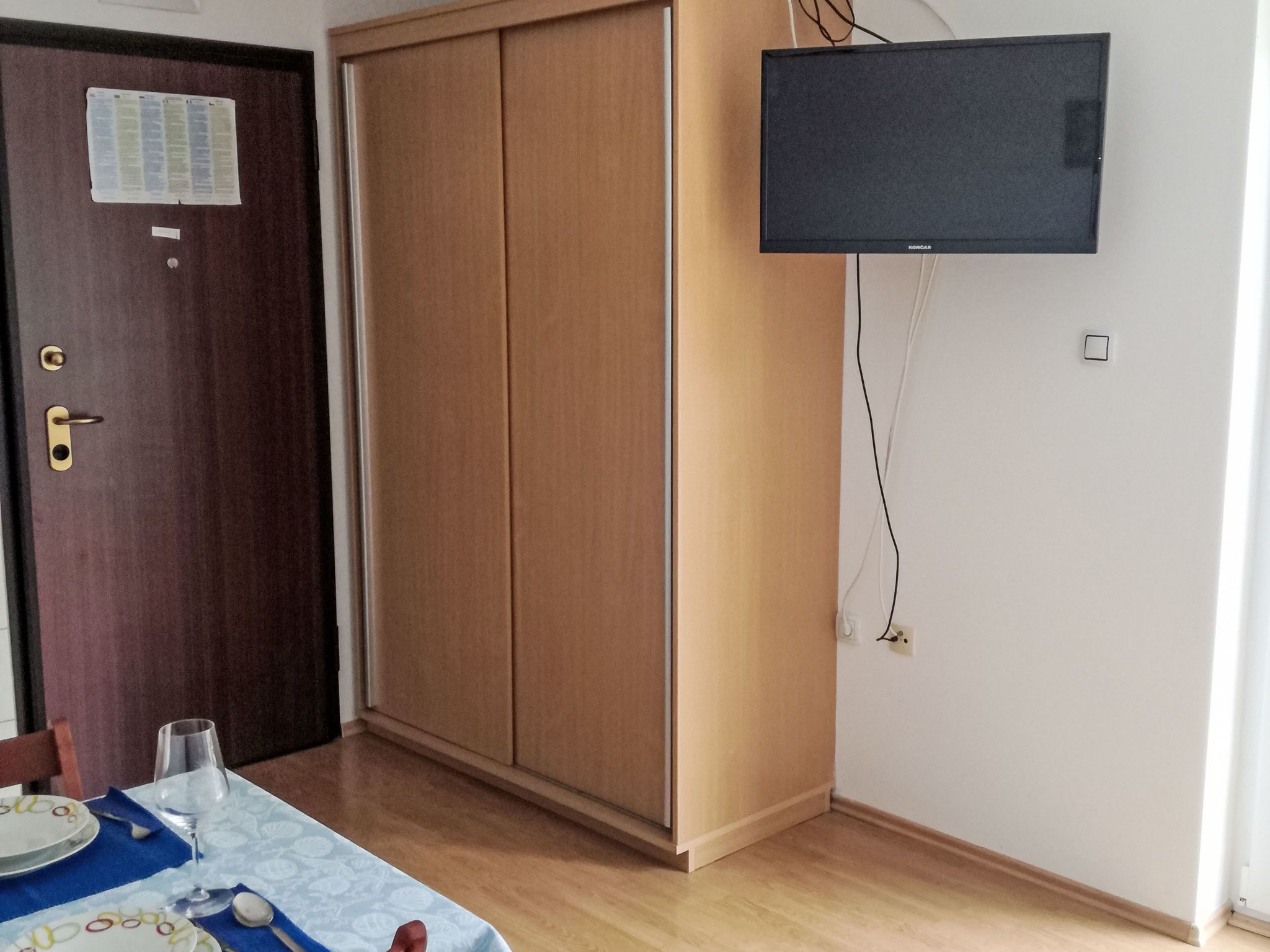 Una habitación con un armario de madera, una mesa con platos y vasos, y un televisor de pared.