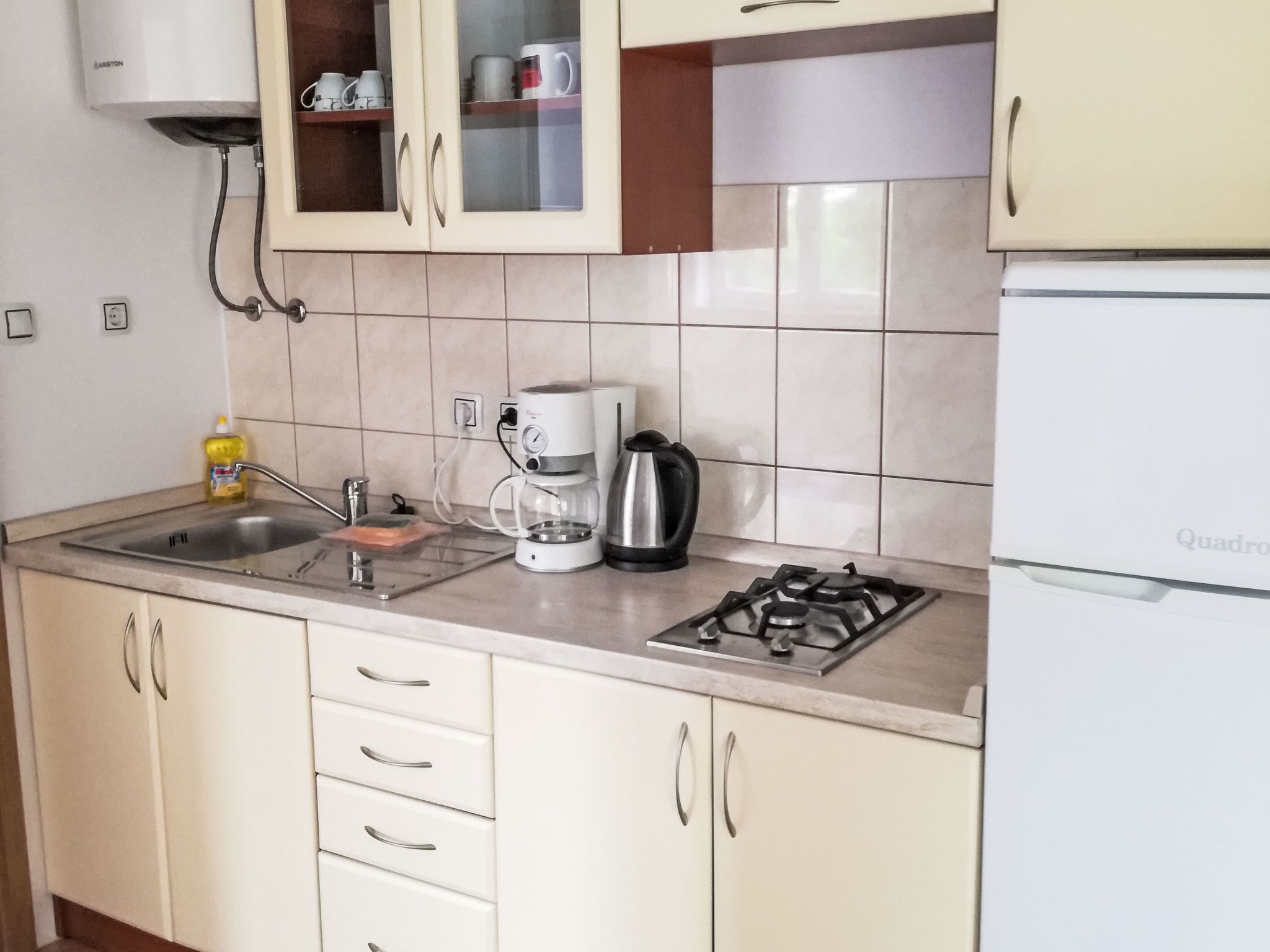 A kitchen with a gas stove, a coffee maker, a sink, and cabinets.