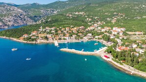 Un pueblo costero con un puerto deportivo, rodeado de colinas y aguas azul turquesa.