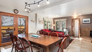 Un comedor amplio con una mesa y sillas de madera, una chimenea y ventanas grandes que ofrecen vistas al exterior.