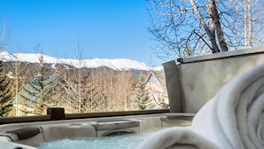Un jacuzzi con vistas a montañas nevadas y árboles desnudos.