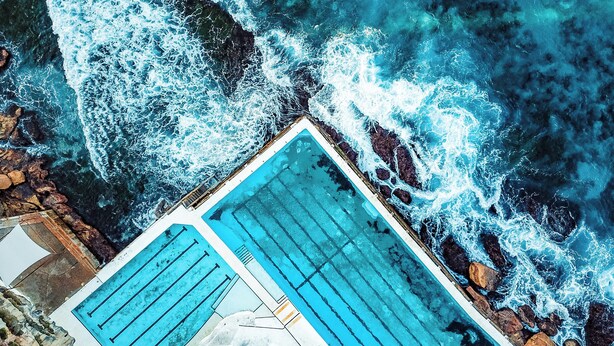 A rooftop pool with a view of the ocean waves crashing onto the shore.