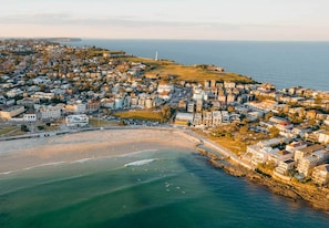Vista aérea de un pueblo costero con playa, edificios residenciales y un faro.