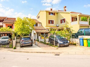 Une rue résidentielle bordée de maisons, avec des voitures garées et un ciel dégagé.