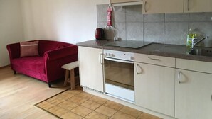 Una cocina compacta con horno integrado, un lavamanos y un hervidor rojo sobre la encimera.