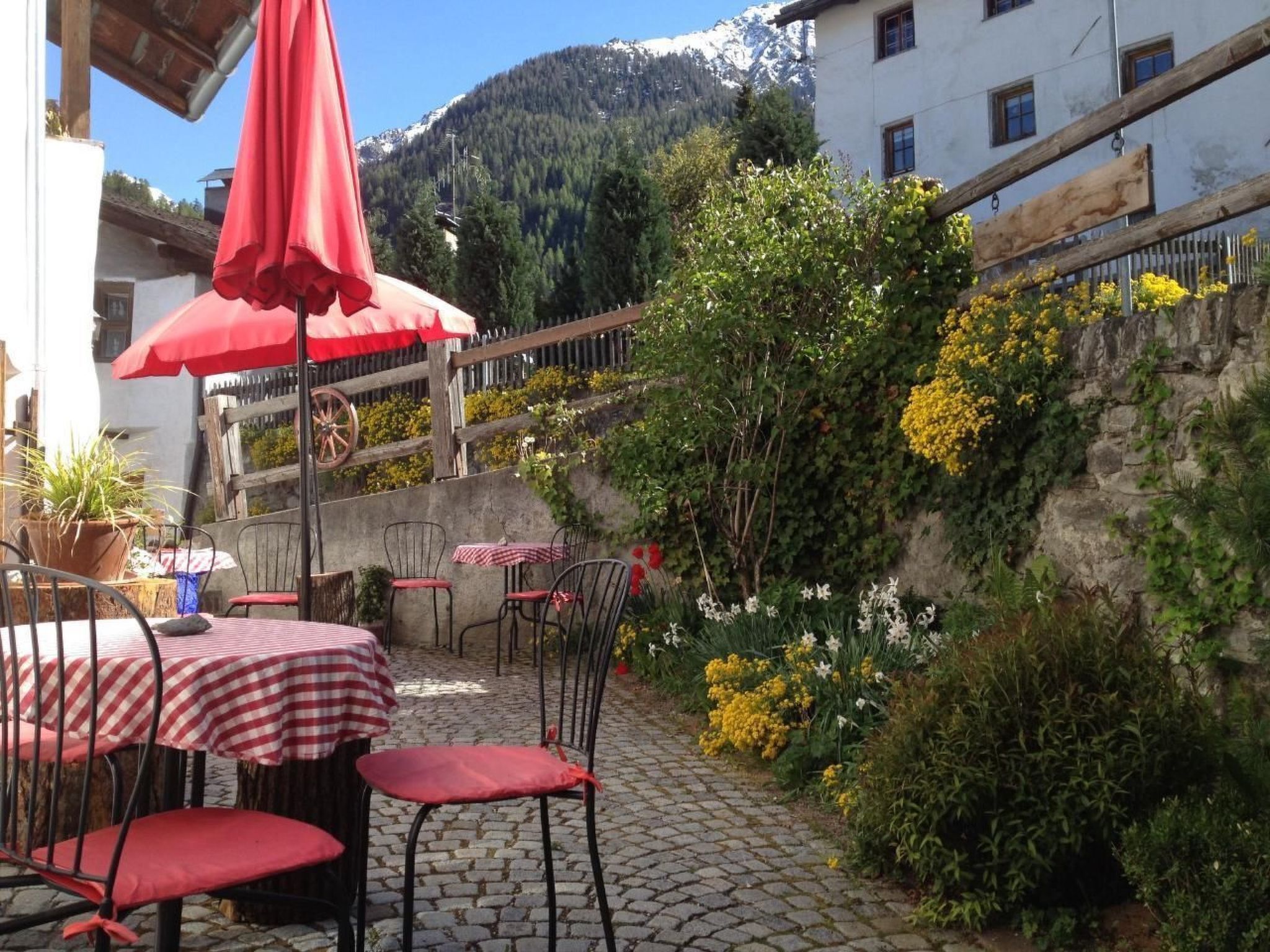 An outdoor café with tables and chairs, surrounded by greenery and a mountain backdrop.