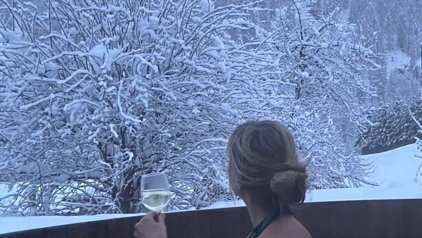 Una persona en un jacuzzi con un paisaje nevado al fondo.