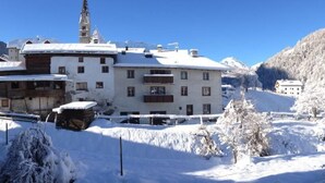 Un edificio cubierto de nieve con múltiples ventanales y balcones, rodeado de árboles nevados y un cielo azul despejado.