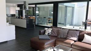 Ein modernes Wohnzimmer mit einer braunen Ledersofa, einem Glastisch und einer Küche im Hintergrund.