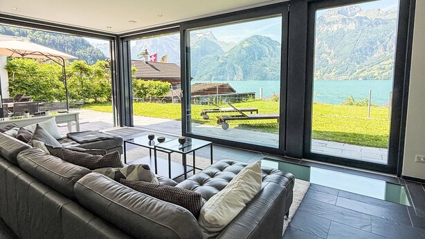 Ein modernes Wohnzimmer mit großem Fenster mit Blick auf einen See und Berge.