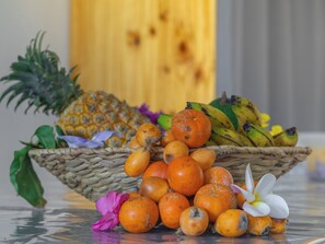 A wicker basket filled with various fruits including oranges, bananas, and a pineapple, placed on a reflective surface. - Studio Paille en ké close to all amenities (C.H.U, IUT, BEACH) (Saint pierre)