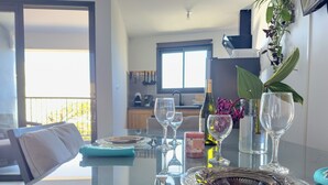Mesa de comedor servida con platos, vasos y una vela en una cocina moderna con vistas al exterior.