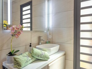 A bathroom with a white sink, a mirror, and a window with blinds. There is a towel with a bird design and a small potted plant on the counter. - Studio Paille en ké close to all amenities (C.H.U, IUT, BEACH) (Saint pierre)