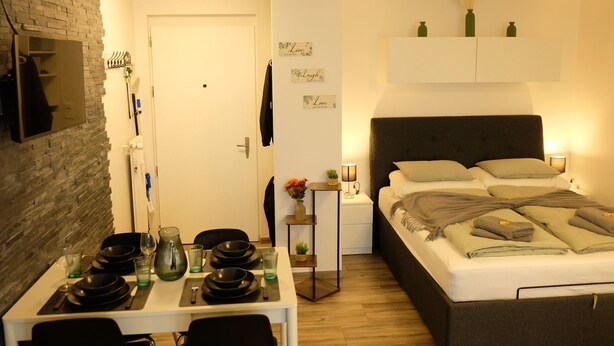 Un dormitorio pequeño con cama, mesita de noche y una pequeña mesa con vajilla.