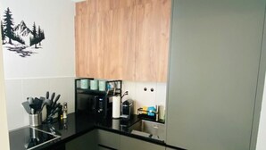 Una cocina compacta con encimera negra, armarios de madera y refrigerador de acero inoxidable.