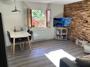 Ein modernes Wohnzimmer mit Essbereich, einem an einer Holzwand montierten Fernseher und einem Fenster mit geöffneter Tür.