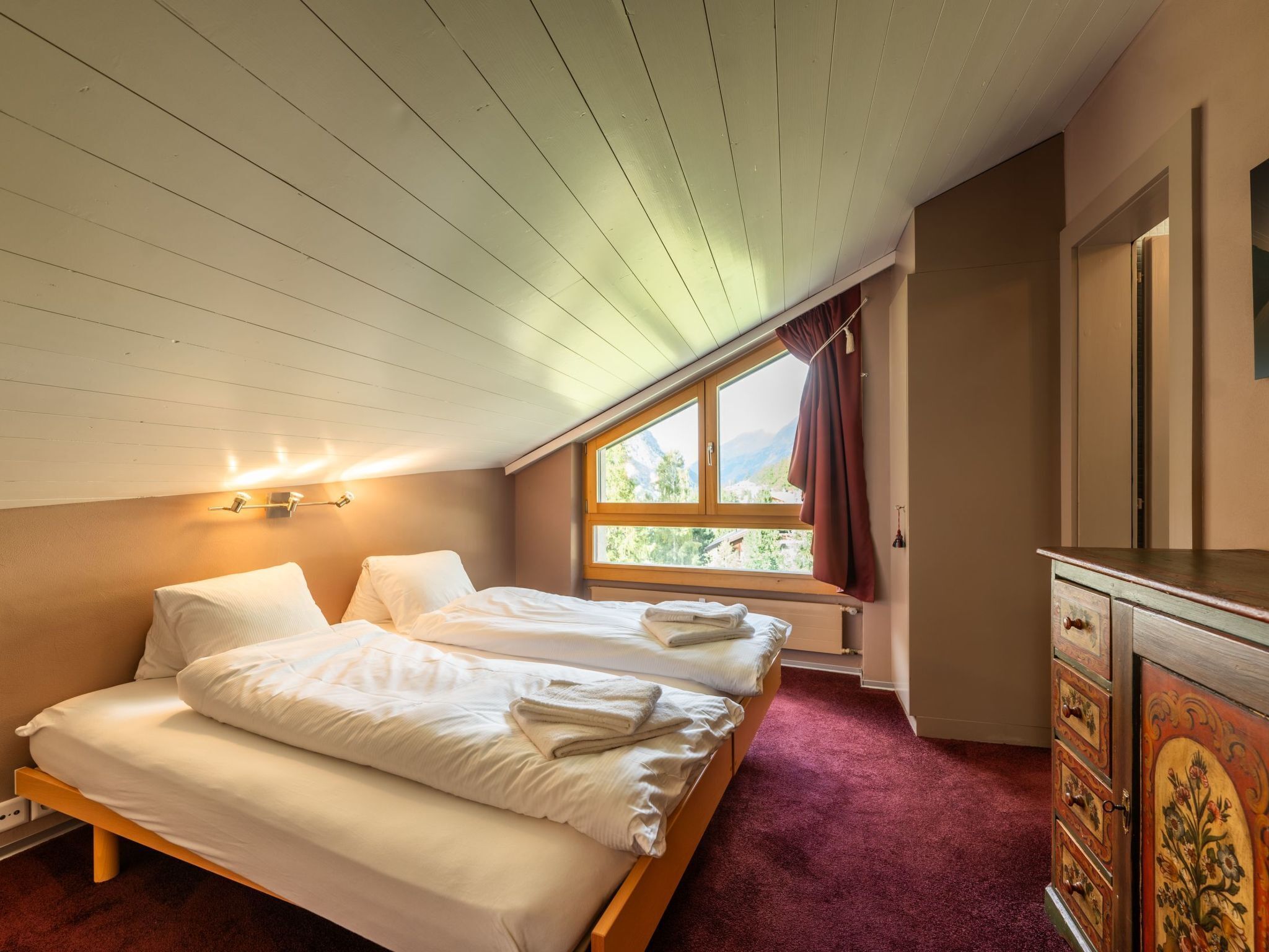 A bedroom with two beds, a window with a view of mountains, a radiator, and a dresser with drawers.