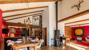 Um interior rústico com mesa de jantar de madeira, cadeiras de pele, lareira e uma parede com detalhes em vermelho.