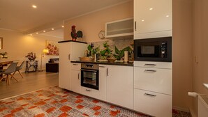 Une cuisine moderne avec des armoires blanches, un four à micro-ondes et un four traditionnel. On y trouve un coin repas avec une table et des chaises, ainsi qu’un coq décoratif accroché au mur.