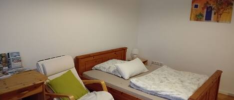 Una habitación pequeña y acogedora con una cama de madera, una silla con un cojín verde, un escritorio con una lámpara y un cuadro en la pared.