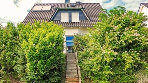 Ein Haus mit einem Ziegeldach, einer Satellitenschüssel und einer Holztreppe, die zu einer blauen Tür führt.
