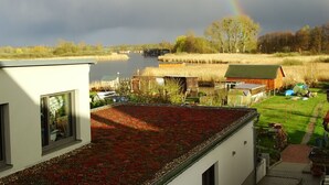 A modern house with a red roof garden, a view of a river, and a rainbow in the distance. - Gemütliches Dachgeschoss-Apartement mit Seeblick und großem Garten am Wasser by Interhome (Ludorf)