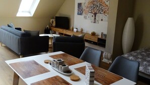 A modern living room with a dining area, featuring a loft-style ceiling, a large window, and a wall-mounted TV. - Gemütliches Dachgeschoss-Apartement mit Seeblick und großem Garten am Wasser by Interhome (Ludorf)