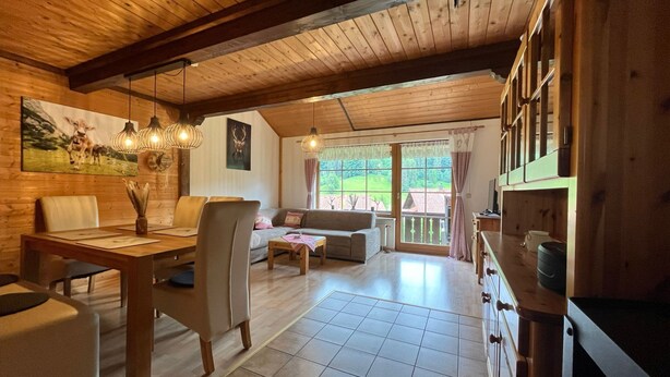 Un intérieur de chalet chaleureux avec un coin repas, un canapé et une vue sur l’extérieur grâce à de grandes fenêtres.
