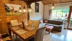 Un coin repas chaleureux avec une table et des chaises en bois, un canapé et une grande fenêtre donnant sur l’extérieur.