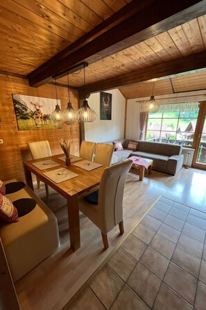 Ein gemütlicher Essbereich mit Holztisch und -stühlen, einer Couch und einem großen Fenster mit Blick ins Freie.