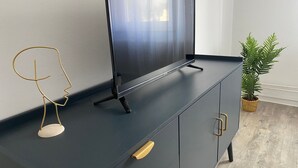 Moderni olohuone, jossa on seinälle asennettu taulutelevisio tummanvärisessä kaapissa, kultainen metallilankaesine ja ruukussa oleva kasvi.