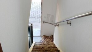Eine Holztreppe mit Metallgeländer, weißen Wänden und einem Fenster am Obergeschoss.