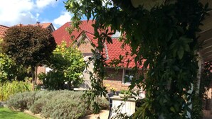 Een bakstenen huis met een rood dak, omgeven door een verzorgde tuin met diverse planten en een pad dat leidt naar een patio.