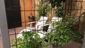 Ett inhägnat utomhusområde med två krukväxter och en stol med blommiga kuddar.