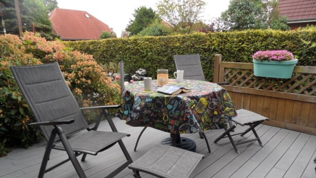 An outdoor patio with a table covered in a tablecloth with doodles, surrounded by four chairs. - Friedel by Interhome (Grossheide)
